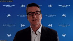 A man in glasses and suit standing next to a blue wall.