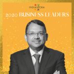 A man with glasses and suit standing in front of a yellow background.