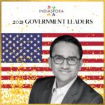 A man in glasses and suit standing next to an american flag.