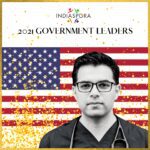 A man in glasses and medical coat standing next to an american flag.