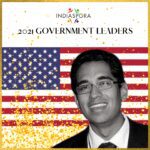 A man in glasses and suit standing next to an american flag.