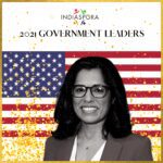 A woman in glasses and a jacket standing next to an american flag.