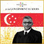 A man in an official gown standing next to the flag of singapore.