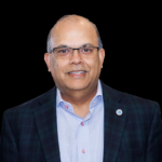 A man in a suit and glasses is smiling.