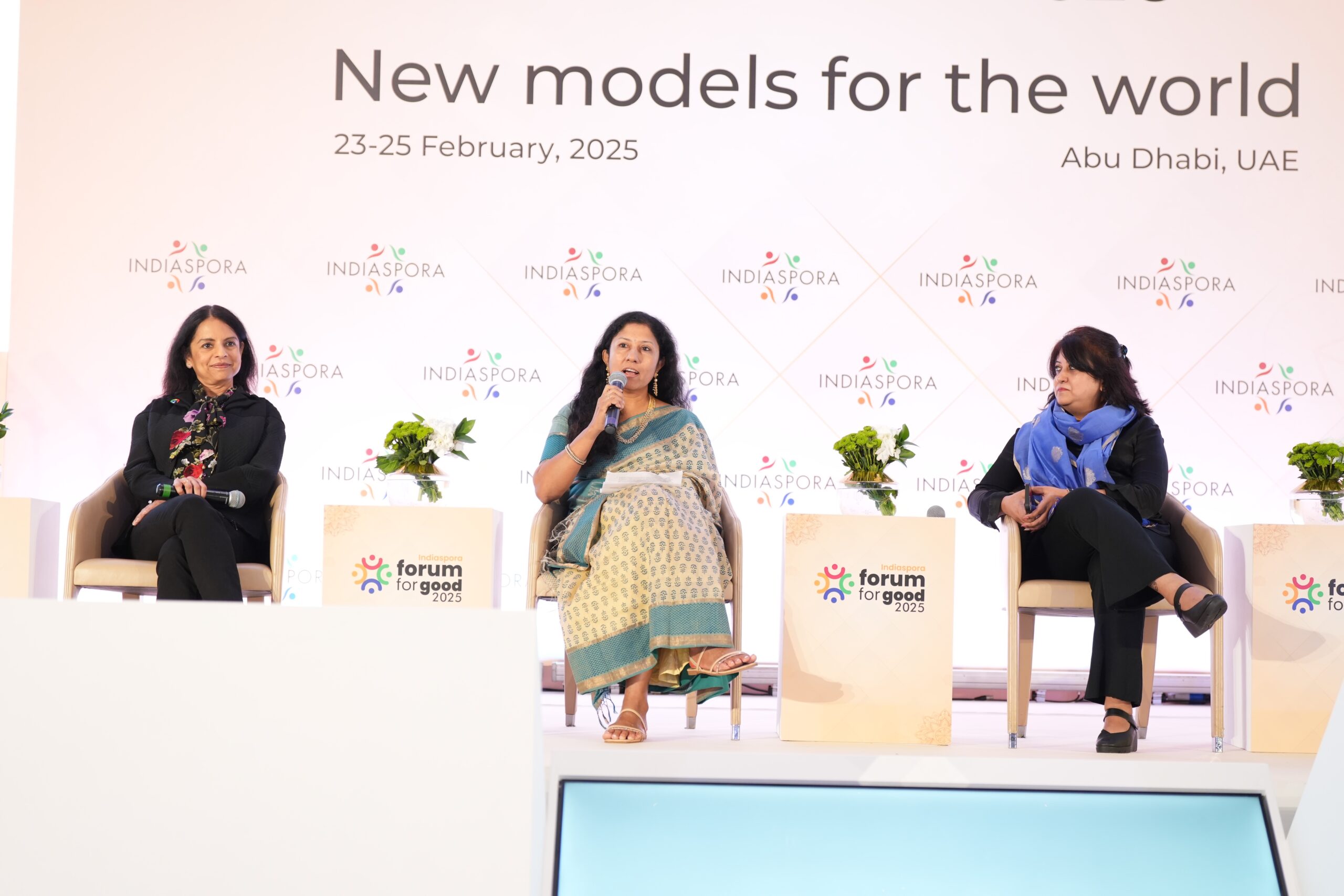Three women are sitting on a stage and one is speaking.