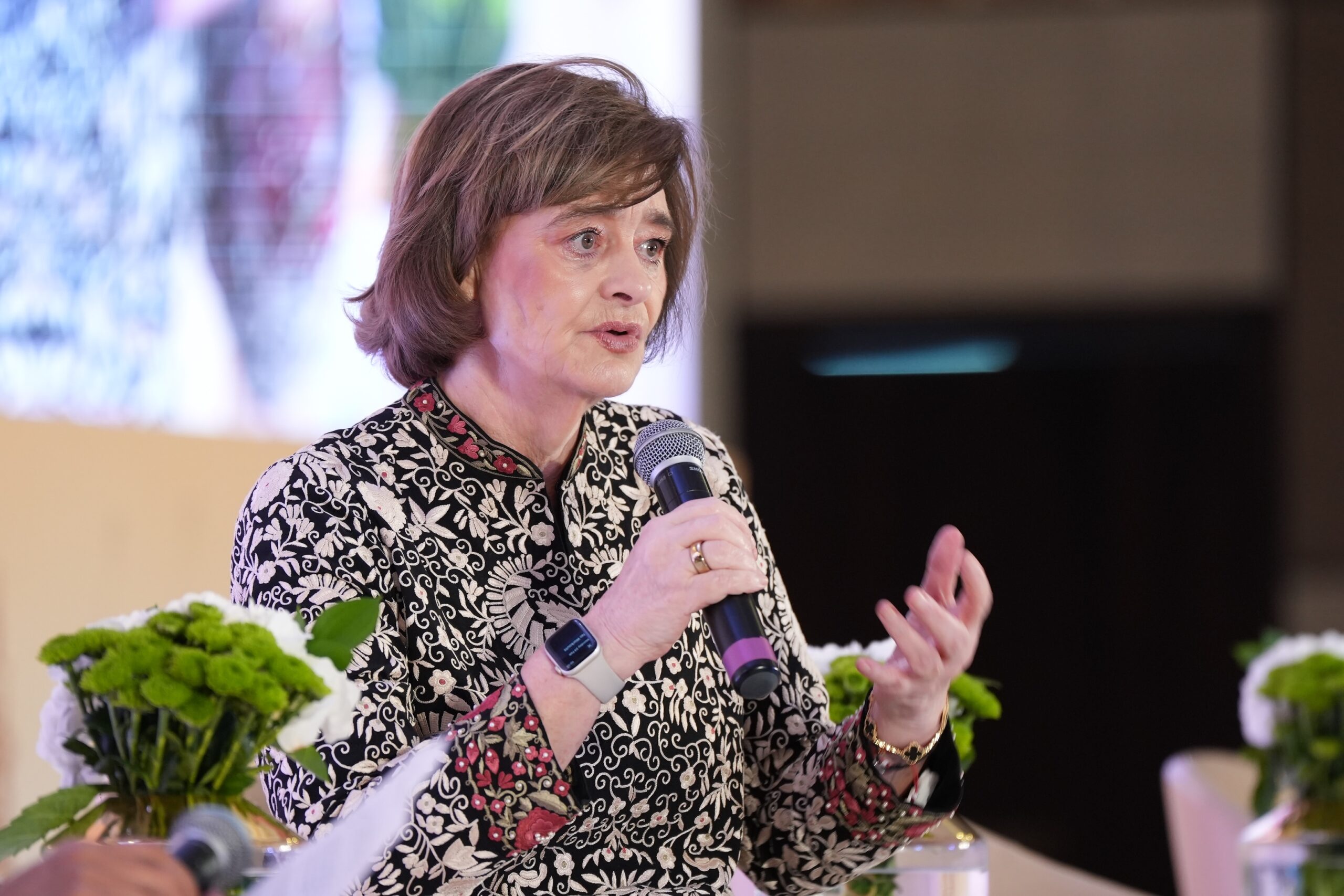 A woman is speaking at an event with flowers.
