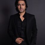 A man in black suit standing next to a wall.