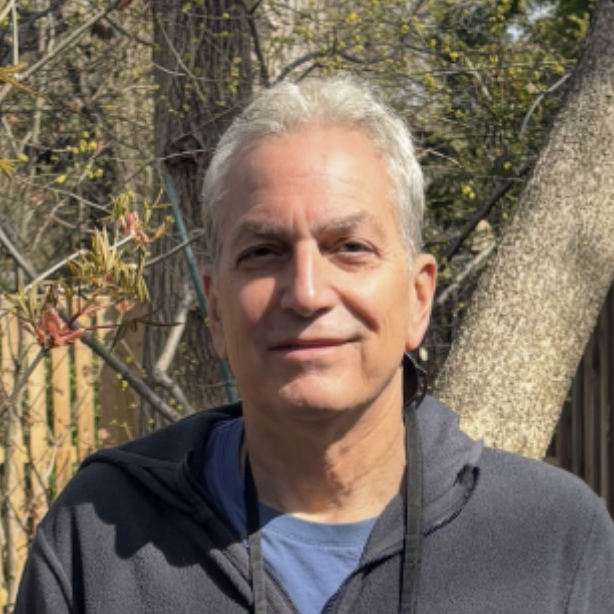 A man with white hair standing in front of a tree.