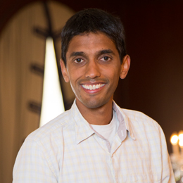 A man smiling for the camera in front of a wall.