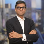 A man in glasses and suit standing with his arms crossed.