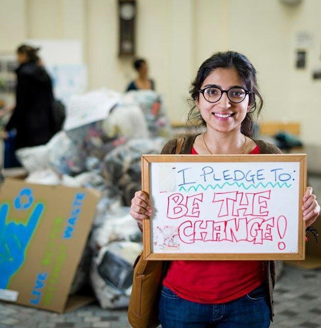 A woman holding up a sign in front of a pile of cardboard.