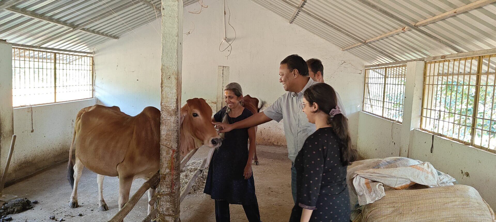 People interacting with a cow in barn.|Group standing in agricultural machinery workshop.|Group of people talking in outdoor setting.|Group holding a welcome banner outside building.