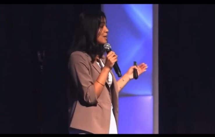 A woman is speaking on stage with a microphone.|A woman holding a blow dryer in her hand.