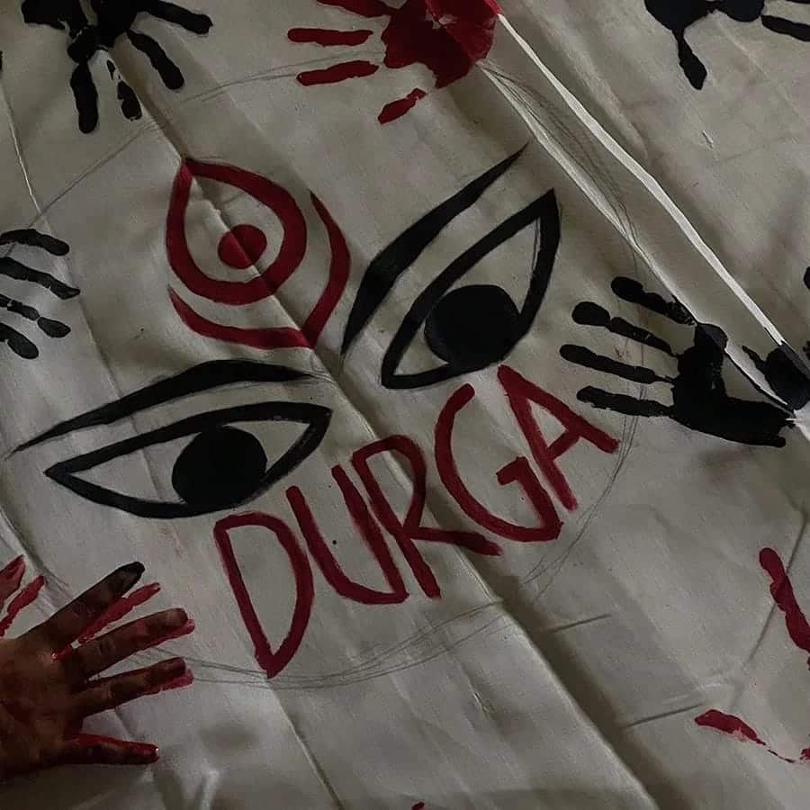 Durga artwork with colorful handprints and eyes.|Stylized Durga eyes logo with text.|Group of women in a meeting outdoors.|People interacting and smiling in colorful uniforms.|Red emergency light and switch panel.|Three people holding certificates outdoors.|Passengers seated inside a public bus.