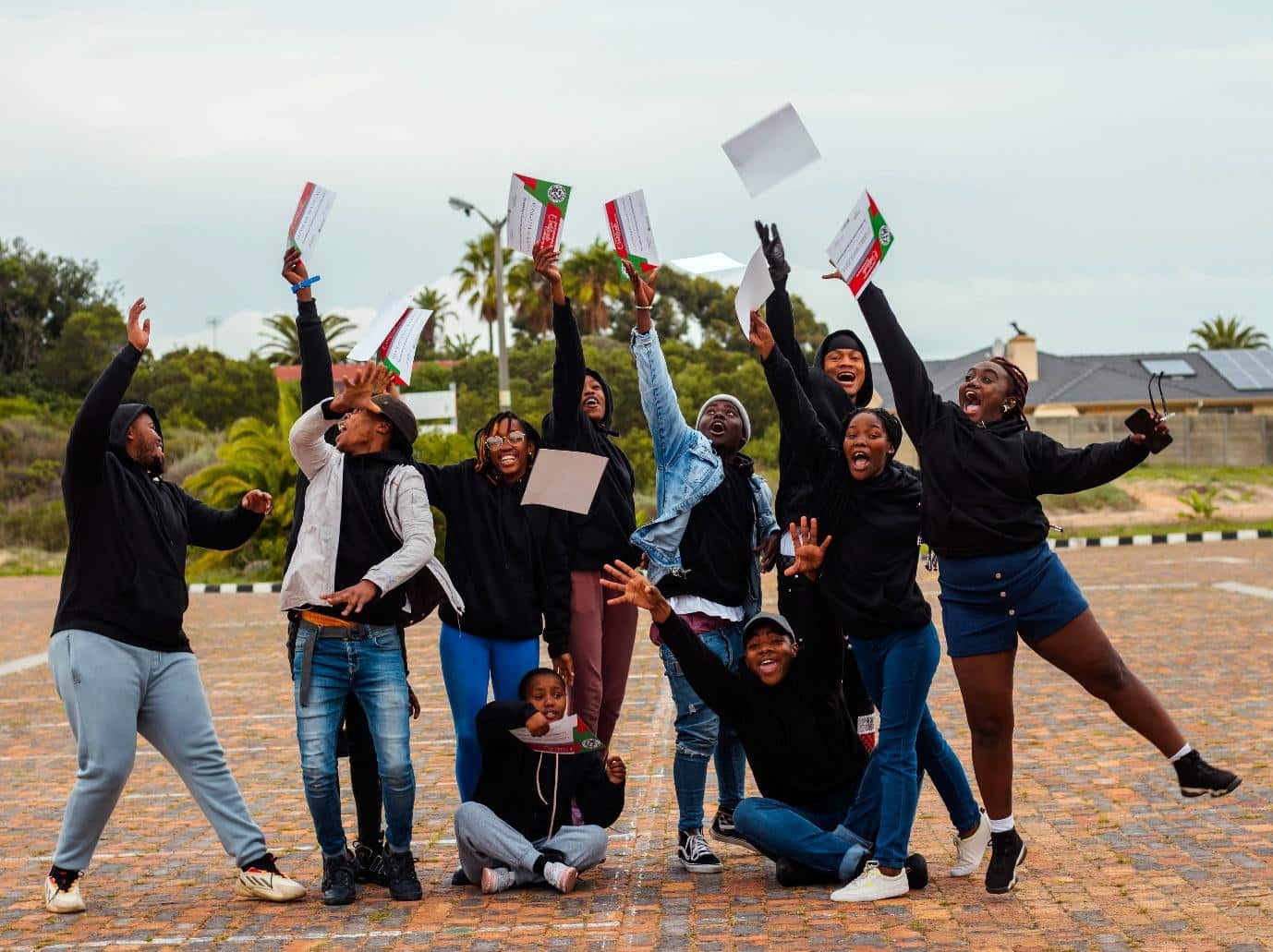 Group celebrating by jumping and throwing papers.|Group of people celebrating outdoors, hands raised.|Woman speaking at an EMpower event.