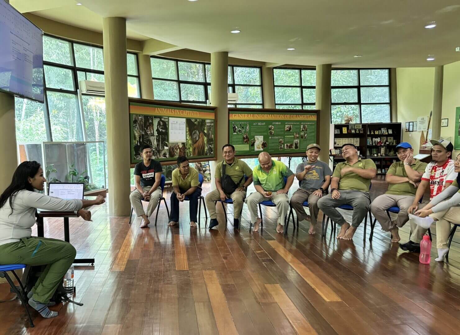 People sitting in a circle during meeting.|Smiling person with long dark hair.|Three friends smiling and posing indoors.|Group photo with people and dogs outside.|Orangutan hanging in lush green forest.|People standing in a room, group meeting.