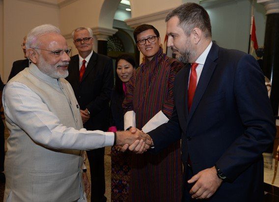 A man in suit and tie shaking hands with an indian person.|A group of people standing on the ground near an airplane.