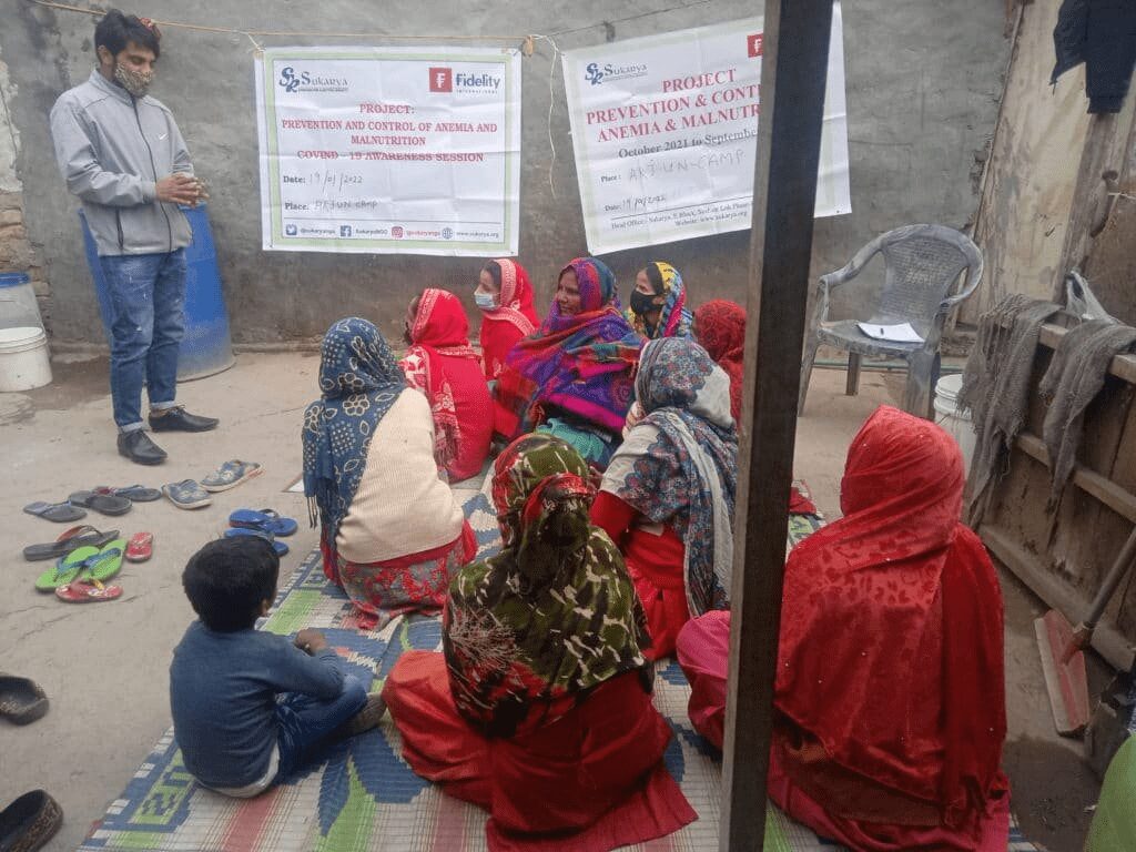 A group of people sitting in front of two boards.|A bar graph showing the number of people who have anaemia in their blood.|A graphic showing the gender gap in india