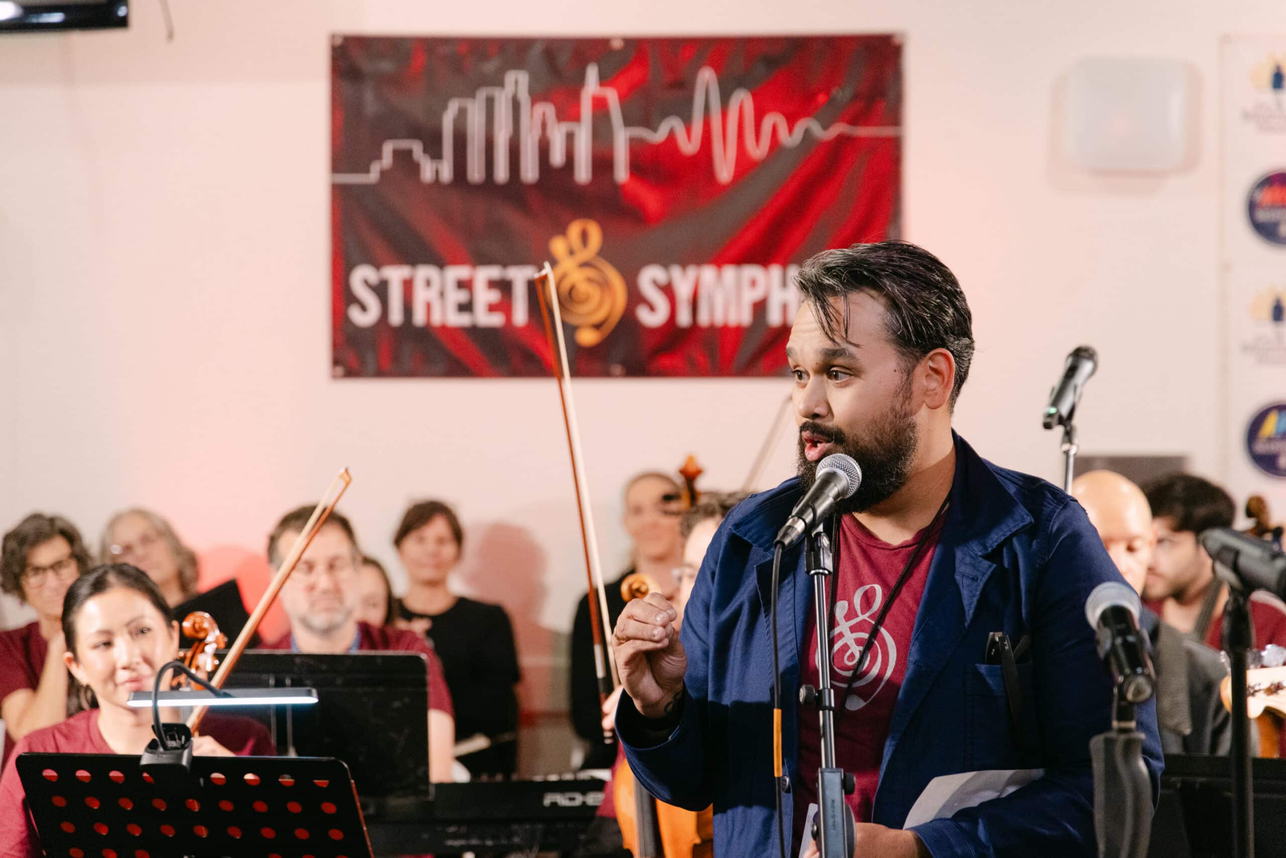 Speaker at Street Symphony concert with musicians|Bearded man holding violin outdoors|Orchestra violinists performing in classical concert|Man holding baby at festive meal table