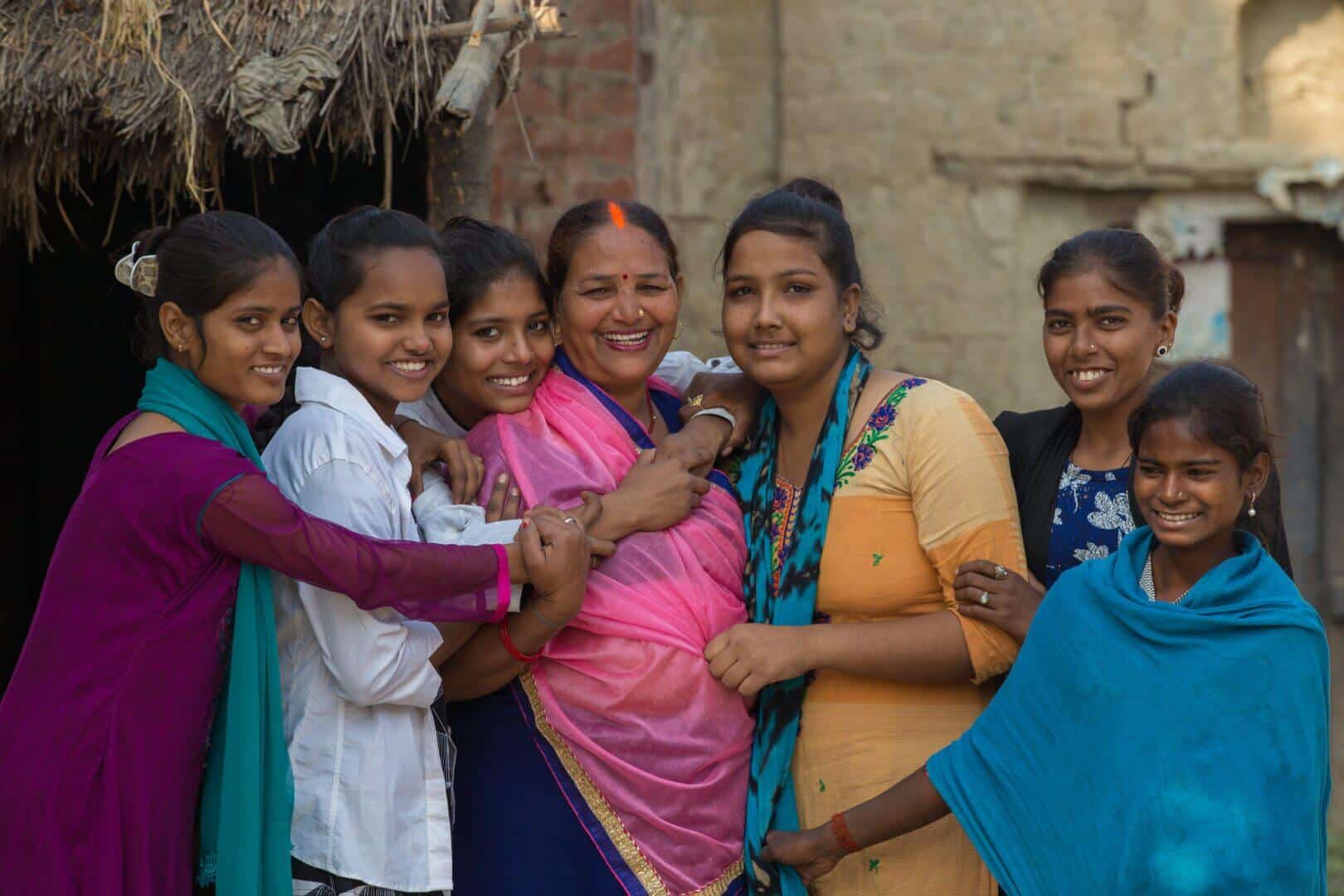Group of smiling women and girls together.|Group of women sitting and talking outside.|Smiling woman standing outdoors with crossed arms.