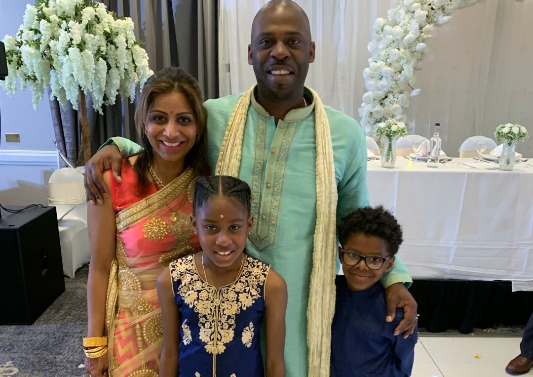 A man and two women posing for a picture with their children.|A man with a blue shirt and jacket on.|A group of people sitting in front of a woman.|A man and woman standing next to a child.