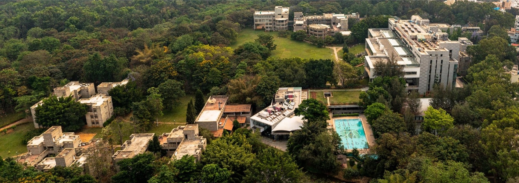 Aerial view of campus with pool and trees|Middle-aged man speaking into handheld microphone|NCBS logo National Centre for Biological Sciences