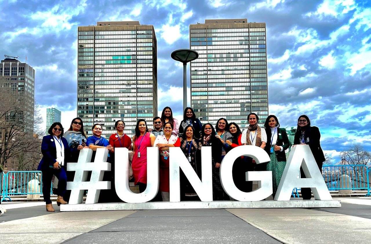 A group of people standing in front of the word " unga ".|A group of people standing in front of the word " unga ".|A group of women standing in front of a wall with black and white checkered floor.|A group of people sitting around a long table.