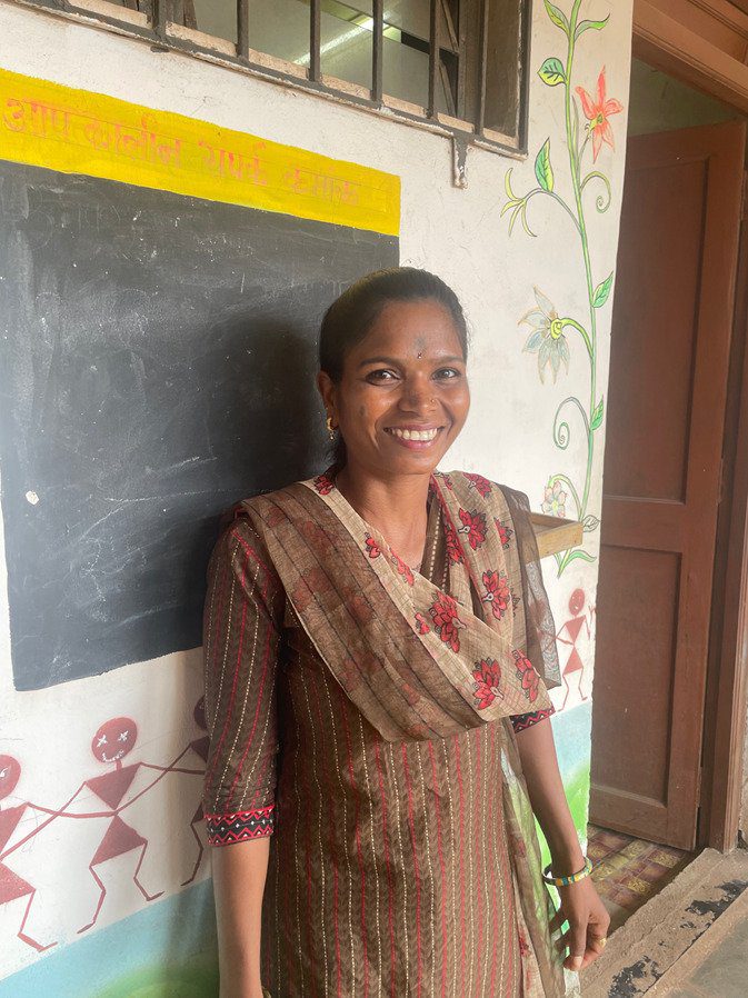 A woman standing in front of a chalkboard.|A bus is driving down the street in front of trees.