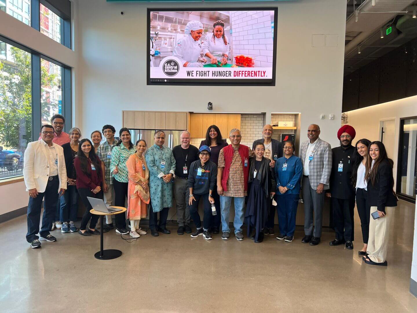 A group of people standing in front of a television.|A woman in a black jacket and blue shirt|A blue and white logo for dharma into action washington dc.