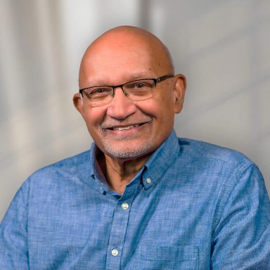 A man with glasses and bald head wearing a blue shirt.
