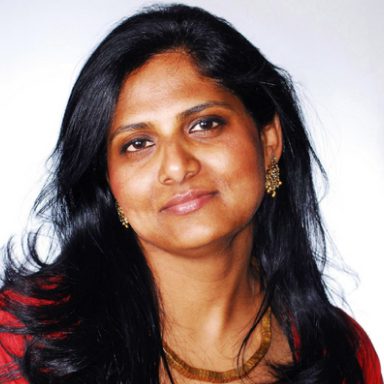 A woman with long black hair wearing gold jewelry.