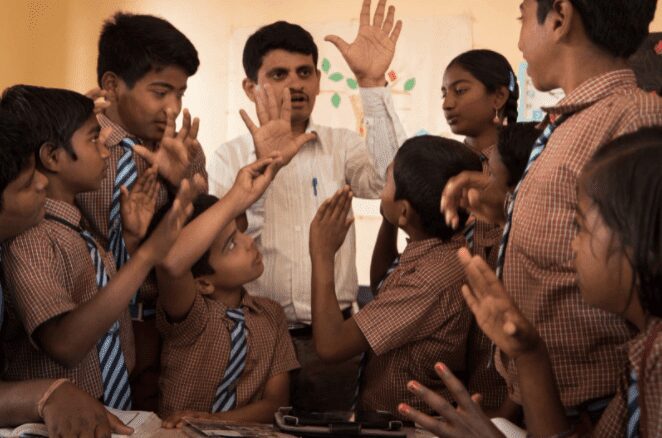 A group of people standing around each other.|A group of people standing around each other.|A group of people in front of a class room.