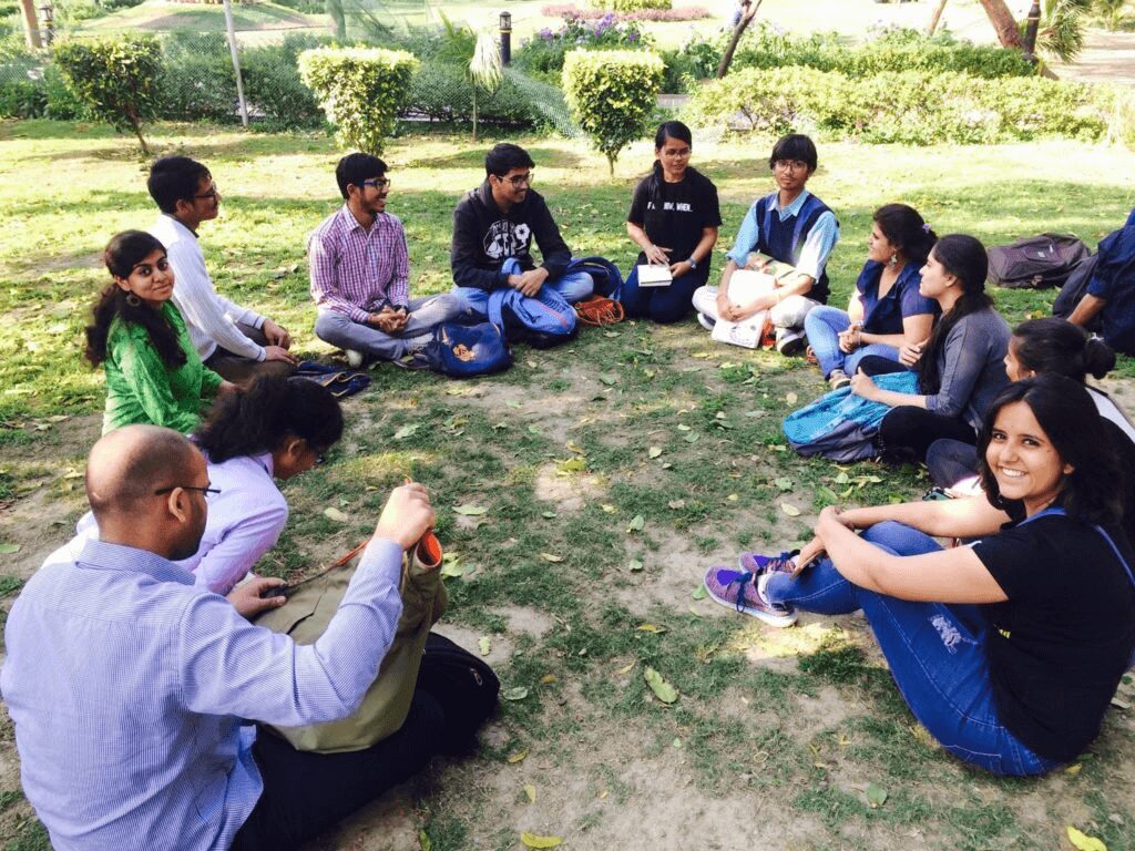 A group of people sitting on the ground in a circle.|A man holding up a sign in front of a wall.