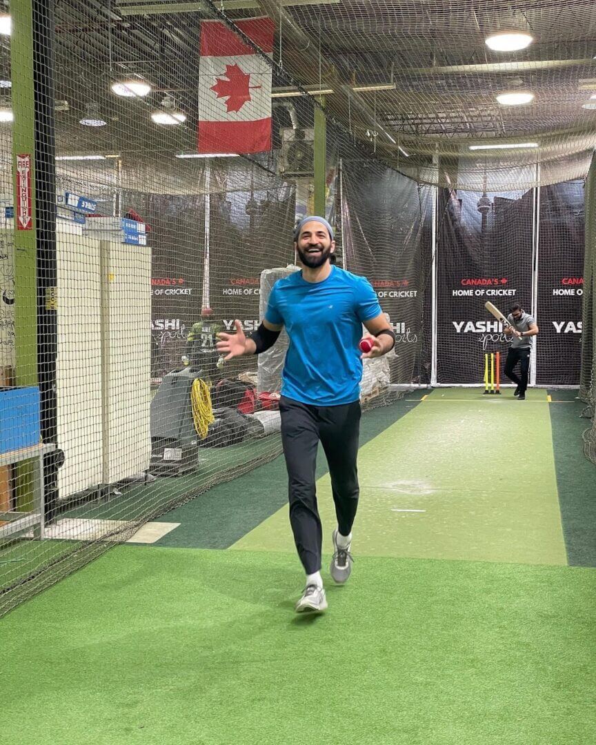 Smiling man running in indoor cricket net|Young bearded man headshot, textured gray background|Athlete kneeling, raising pink ball on practice field