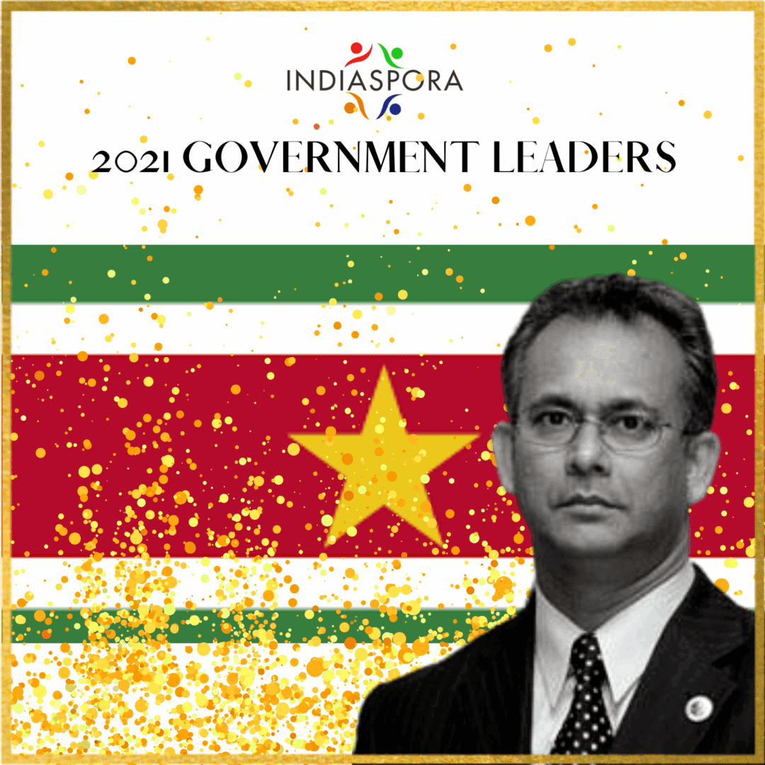 A man in suit and tie next to the flag of suriname.