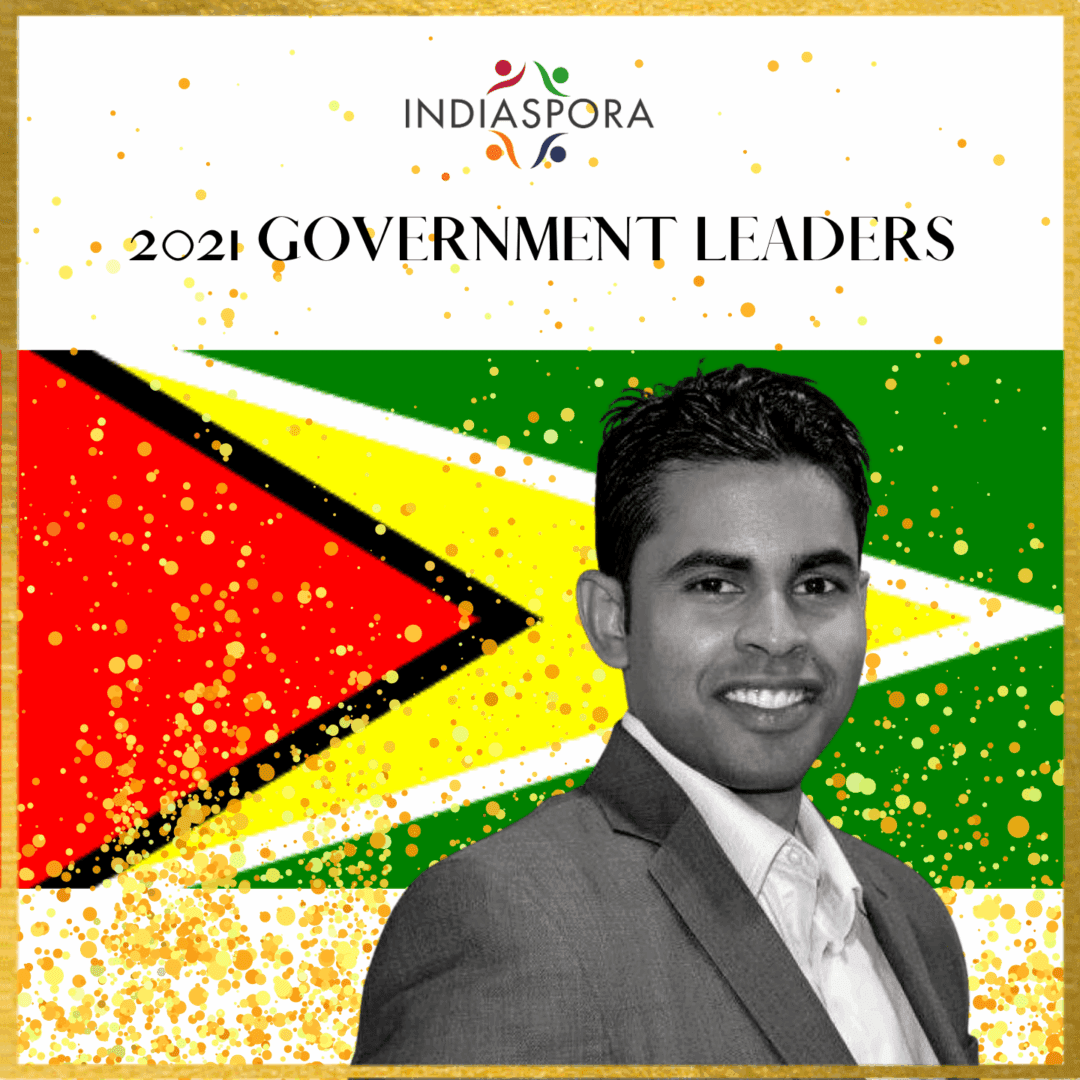 A man in suit and tie standing next to the flag of guyana.