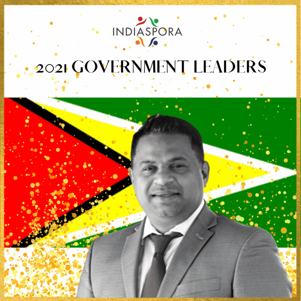 A man in suit and tie standing next to the flag of guyana.