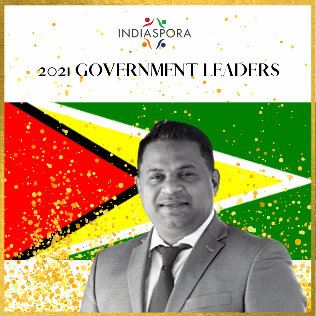 A man in suit and tie standing next to the flag of guyana.