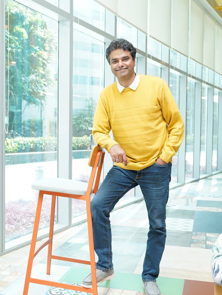 A man in yellow shirt leaning on orange chair.