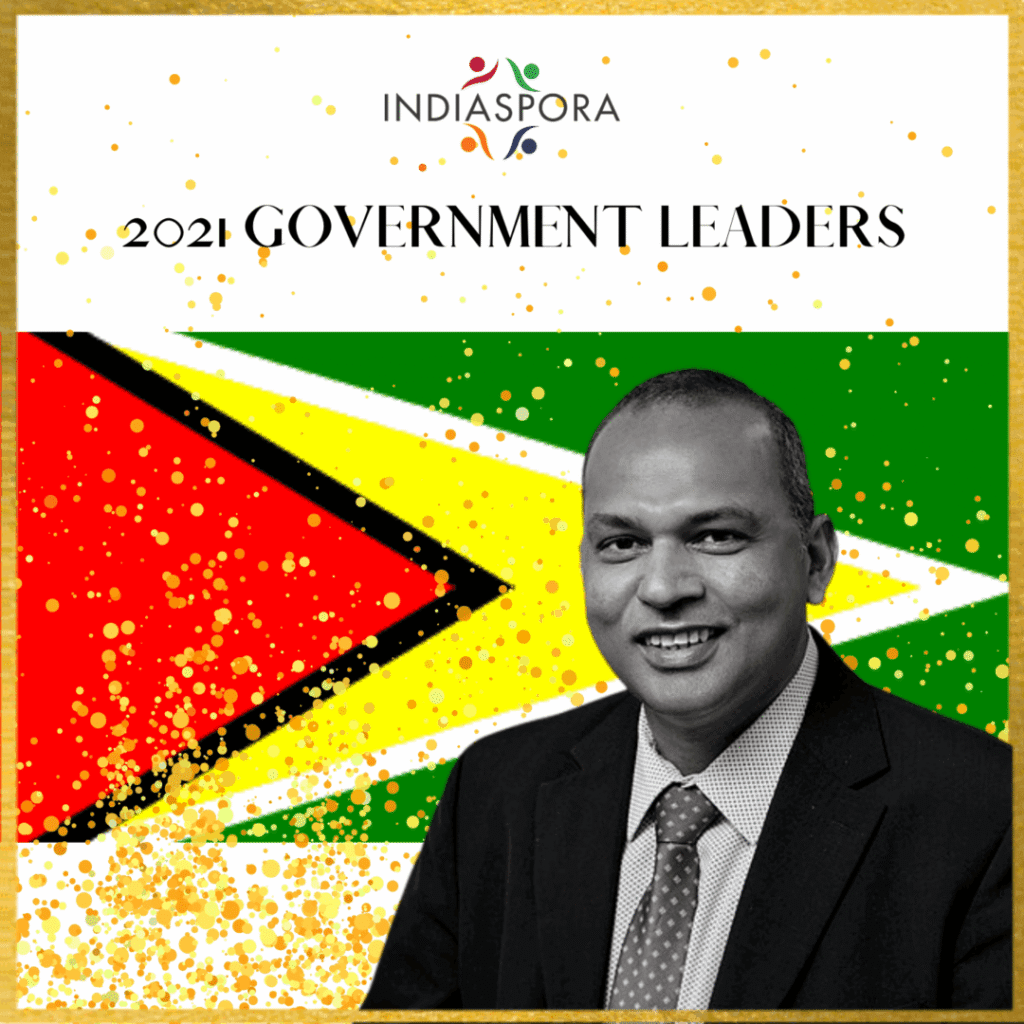 A man in suit and tie next to the flag of guyana.