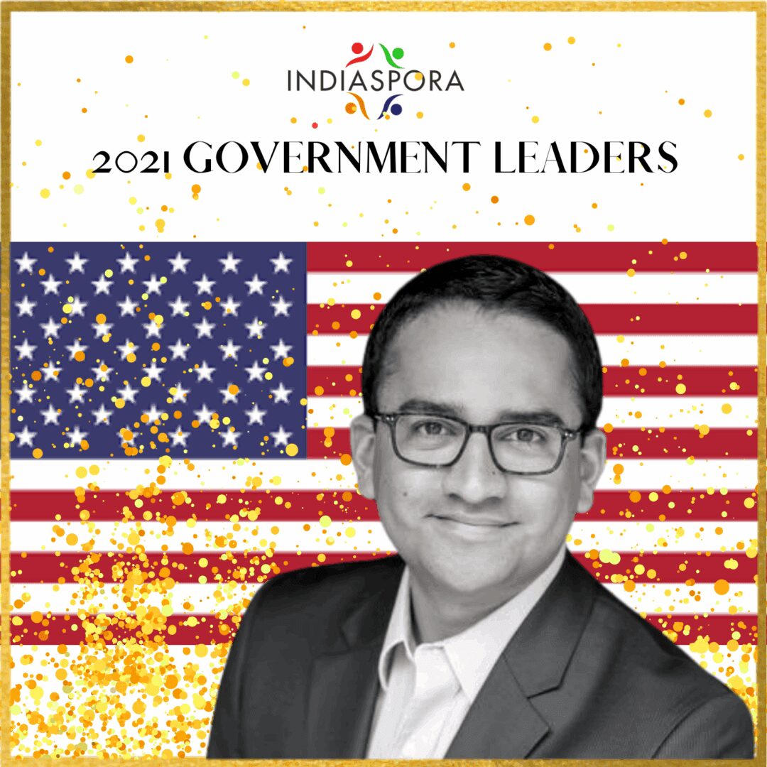 A man in glasses and suit standing next to an american flag.