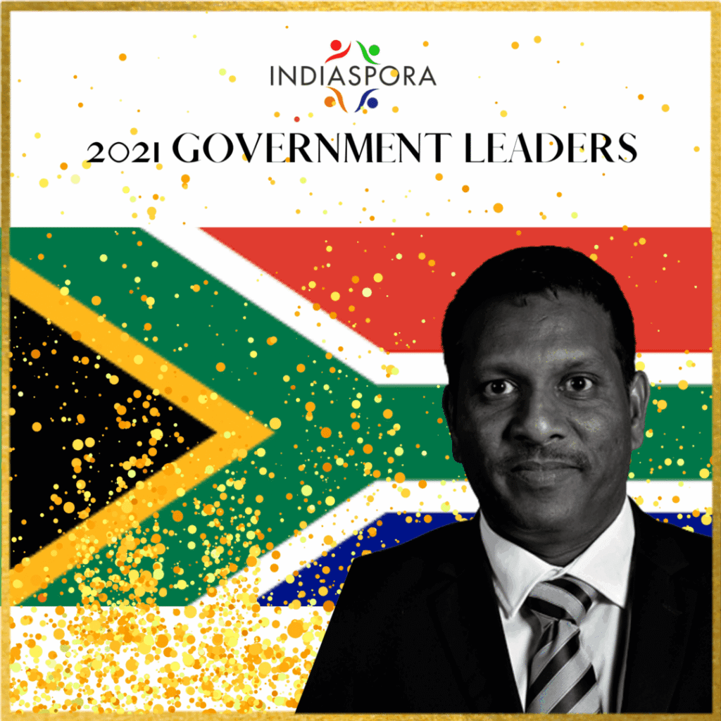 A man in suit and tie standing next to the flag of south africa.