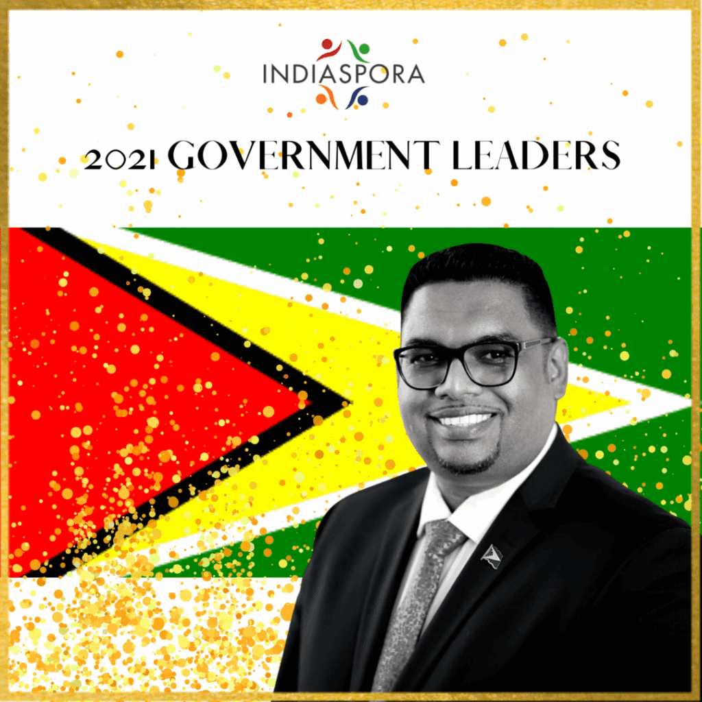 A man in suit and tie standing next to the flag of guyana.|A man in a suit and tie is speaking.|A man in suit and tie standing next to the flag of guyana.