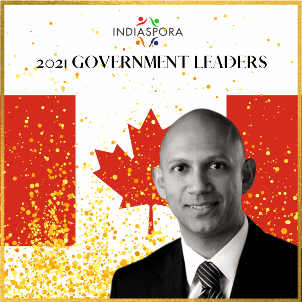 A man in a suit and tie standing next to the canadian flag.