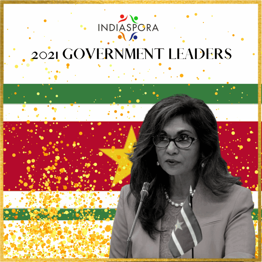 A woman in glasses and tie standing next to a flag.|A woman in glasses and tie standing next to a flag.