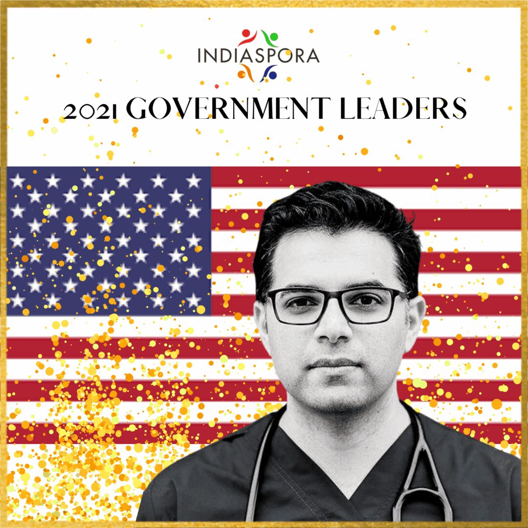 A man in glasses and medical coat standing next to an american flag.