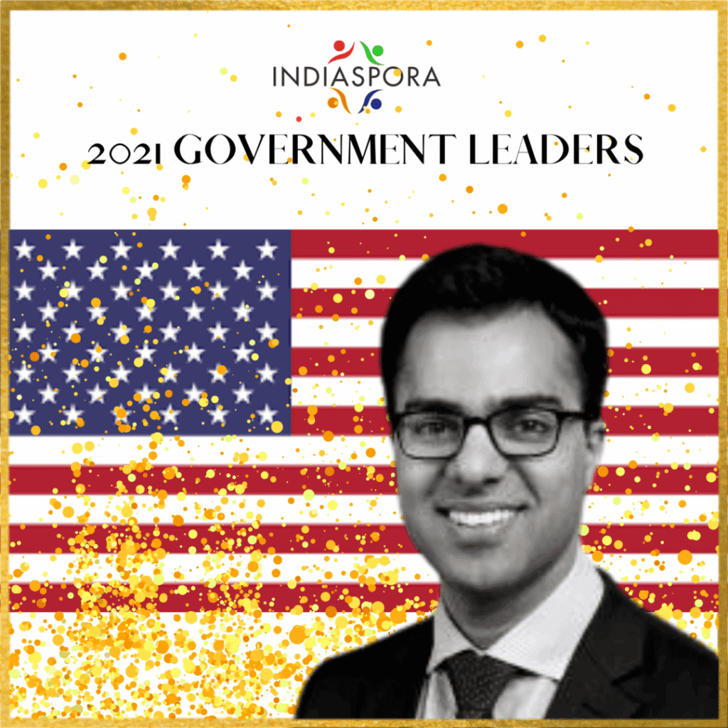 A man in glasses and suit standing next to an american flag.