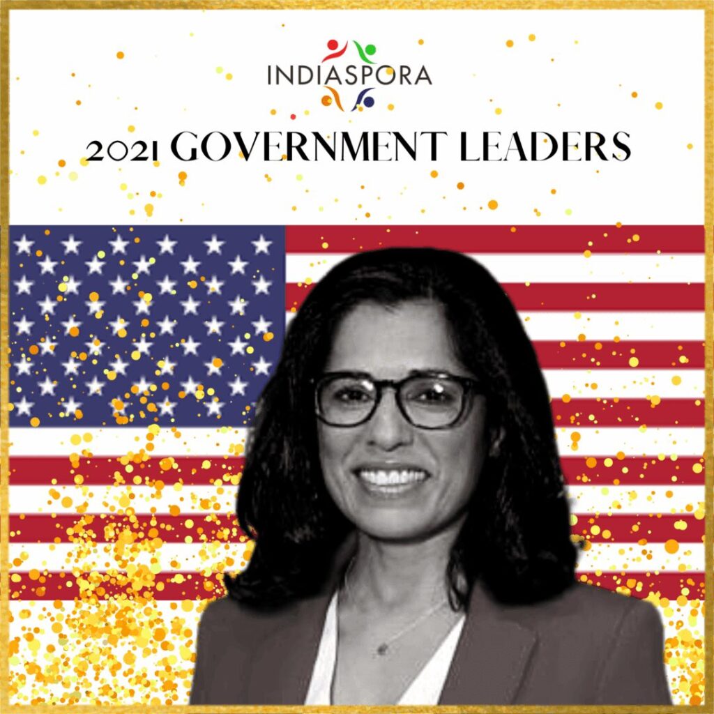 A woman in glasses and a jacket standing next to an american flag.