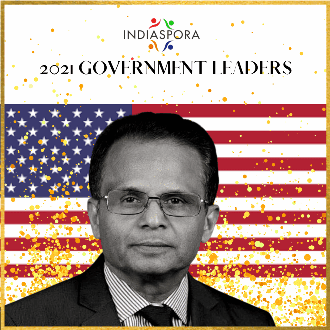A man in glasses and suit standing next to an american flag.