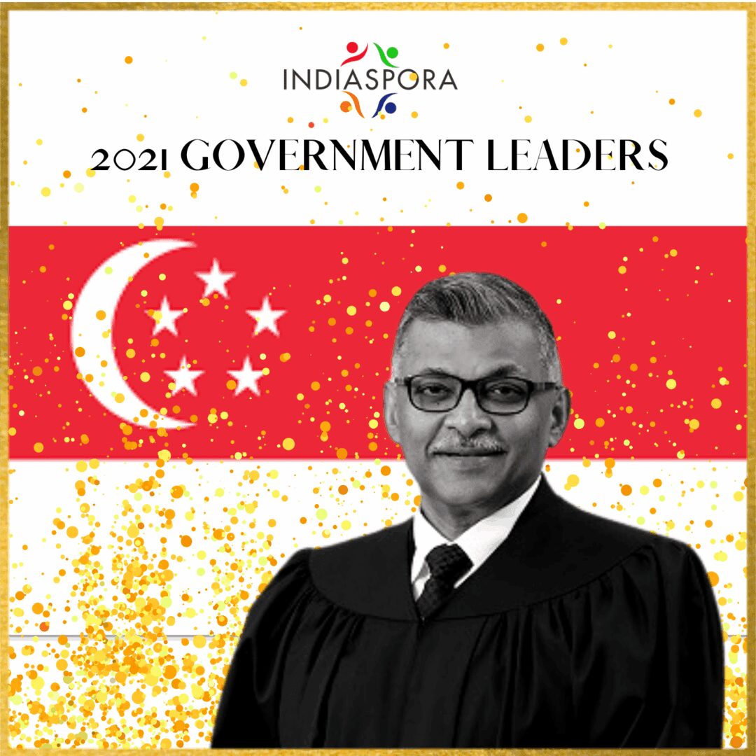 A man in an official gown standing next to the flag of singapore.